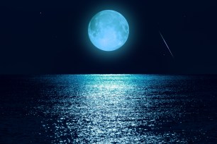 Moon with starry skies above ocean horizon.